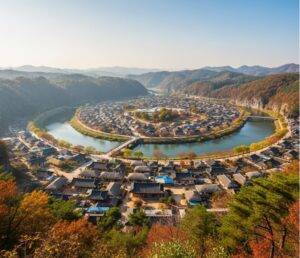 A wide, panoramic aerial view of Andong Hahoe Folk Village, showing its traditional hanok houses nestled within a lush, green river bend under a clear blue sky.