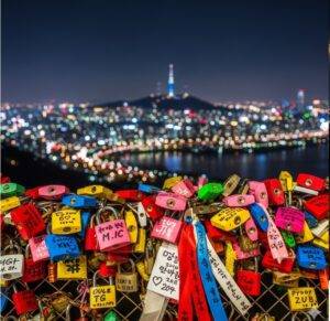 A close-up of colorful love locks on a fence at N Seoul Tower, with the Seoul cityscape blurred in the background.