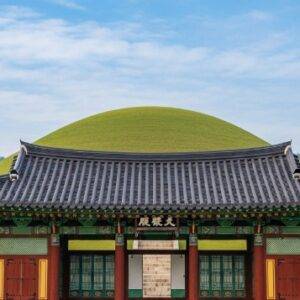 The traditional wooden Jeongjagak memorial shrine at Seonjeongneung, with the grass-covered royal tomb mound visible on the green hill directly behind it.