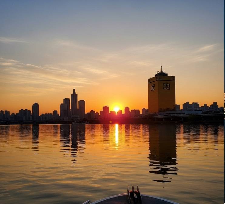 A breathtaking golden hour view of the 63 Building and Yeouido skyline in Seoul, taken from a boat on the Han River during the Sunset Cruise.