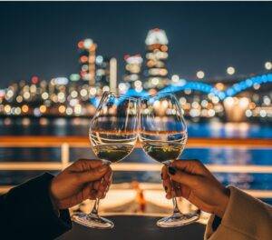 A couple making a romantic toast with wine glasses on a Han River cruise, with the sparkling Seoul skyline in the background.