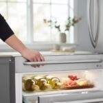 A hand opening the LG LRMVC2306S Full-Convert™ Drawer, revealing chilled white wine bottles and a charcuterie board.