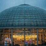 Lotte World Adventure's large glass dome structure glowing warm inside with a carousel, contrasting with the dark, rainy evening in Seoul outside.