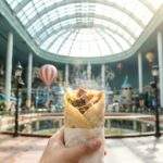 Lotte World Halal Guide: A first-person view holding a delicious Halal chicken kebab wrap inside the bustling Lotte World Adventure indoor theme park under the glass dome ceiling.