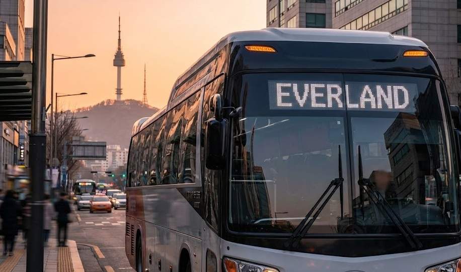 Everland Shuttle Bus from Seoul: A modern tour bus with an "EVERLAND" sign driving on a Seoul street at sunset, with N Seoul Tower in the background.