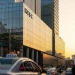 Visiting the HYBE Building: Golden hour photograph of the modern HYBE building in Yongsan, Seoul, contrasted with a busy Korean street scene in the foreground.