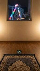 A first-person view inside the quiet Muslim prayer room at Lotte World. A prayer mat is on the floor with a compass app showing Qibla direction. A window in the background shows the bright lights of the theme park rides at night.