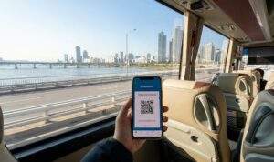 A first-person view from a bus seat, holding a phone with an Everland Shuttle QR code, looking out at the Han River in Seoul.