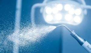 A close-up photograph of a dental scaling tool spraying a fine mist of water, backlit by a clinical light to emphasize cleanliness and advanced technology.