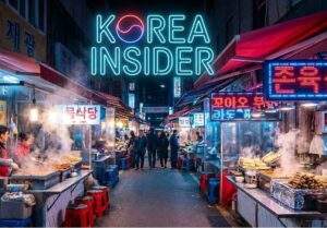 A wide-angle landscape photograph of a bustling Korean night market alley at night. Steam rises from various food stalls lining both sides of the path, and people are walking through. The scene is illuminated by numerous blue and red neon signs with Korean characters. At the top center, a large, glowing neon sign reads "KOREA INSIDER."